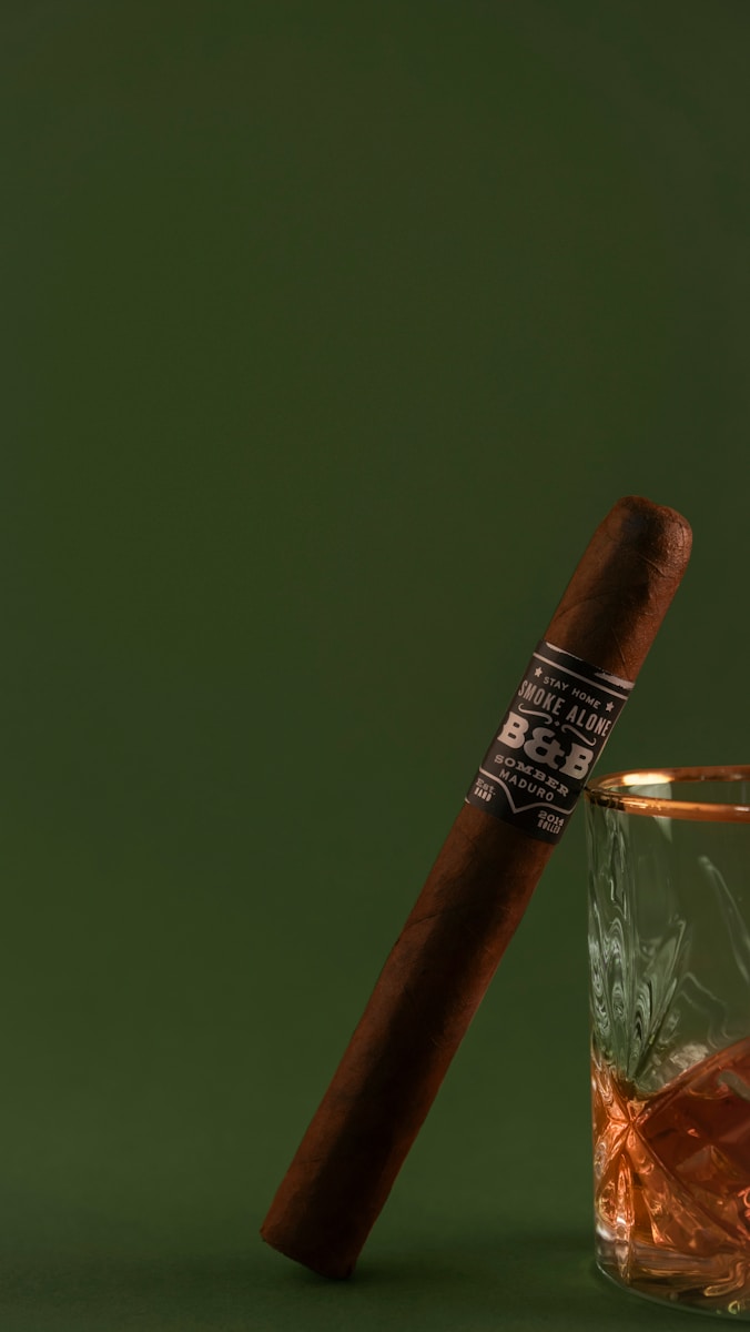 A cigar and a drink on a green background.